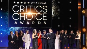 A group of people of varying ethnicities stand on stage. Text on the screen behind them reads "29th ANNUAL CRITICS CHOICE AWARDS."